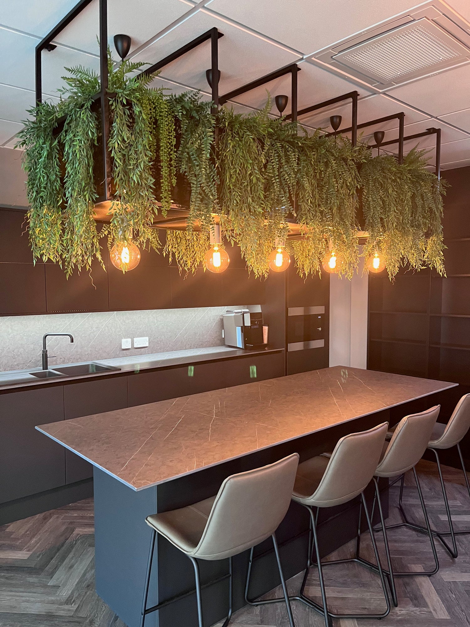 Artificial trailing plants displayed over kitchen island.  Trailing ferns and willow used.