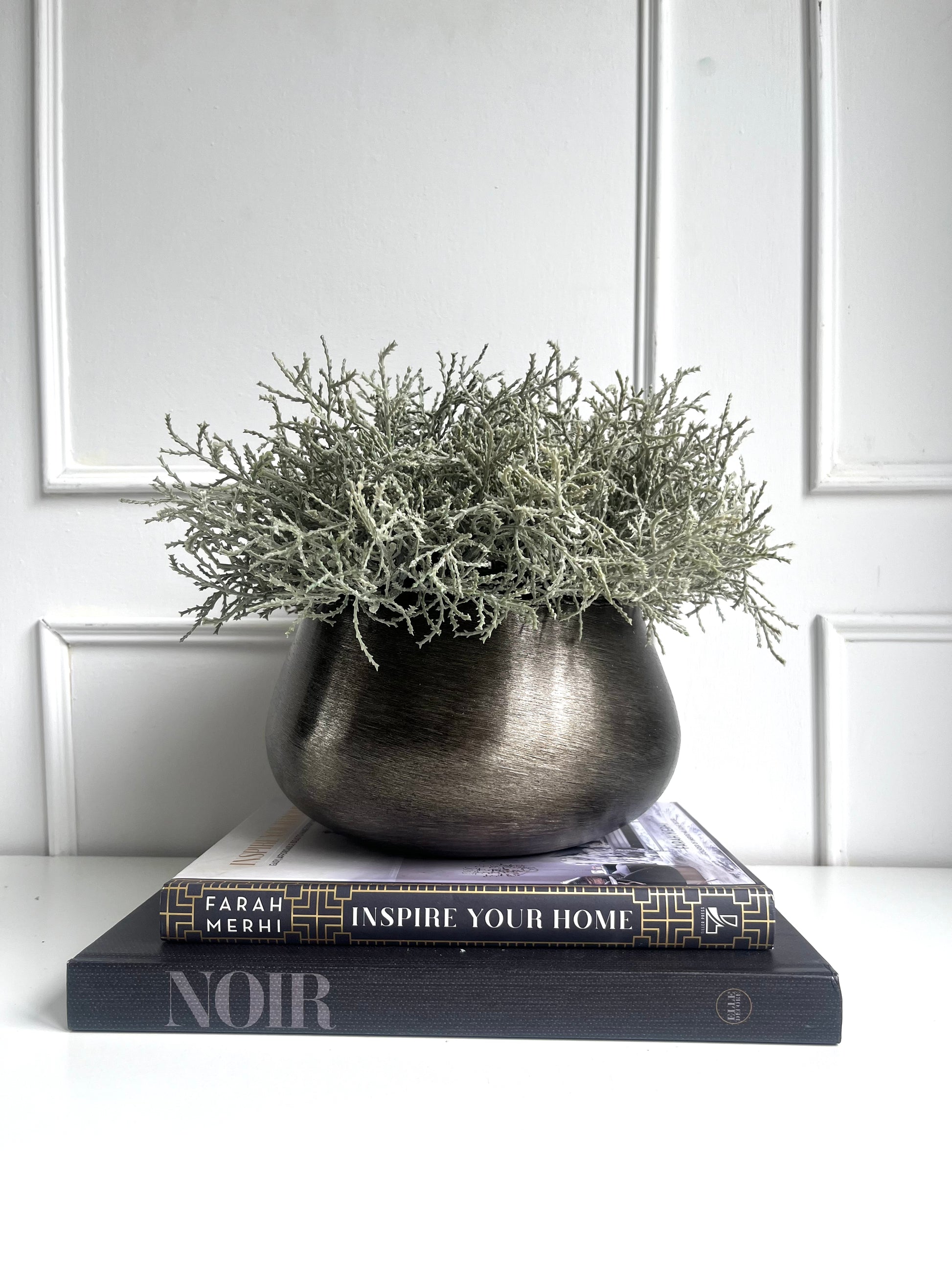 Artificial silver grey santolina arranged in a bronze colour brushed metal planter displayed on a stack of books.