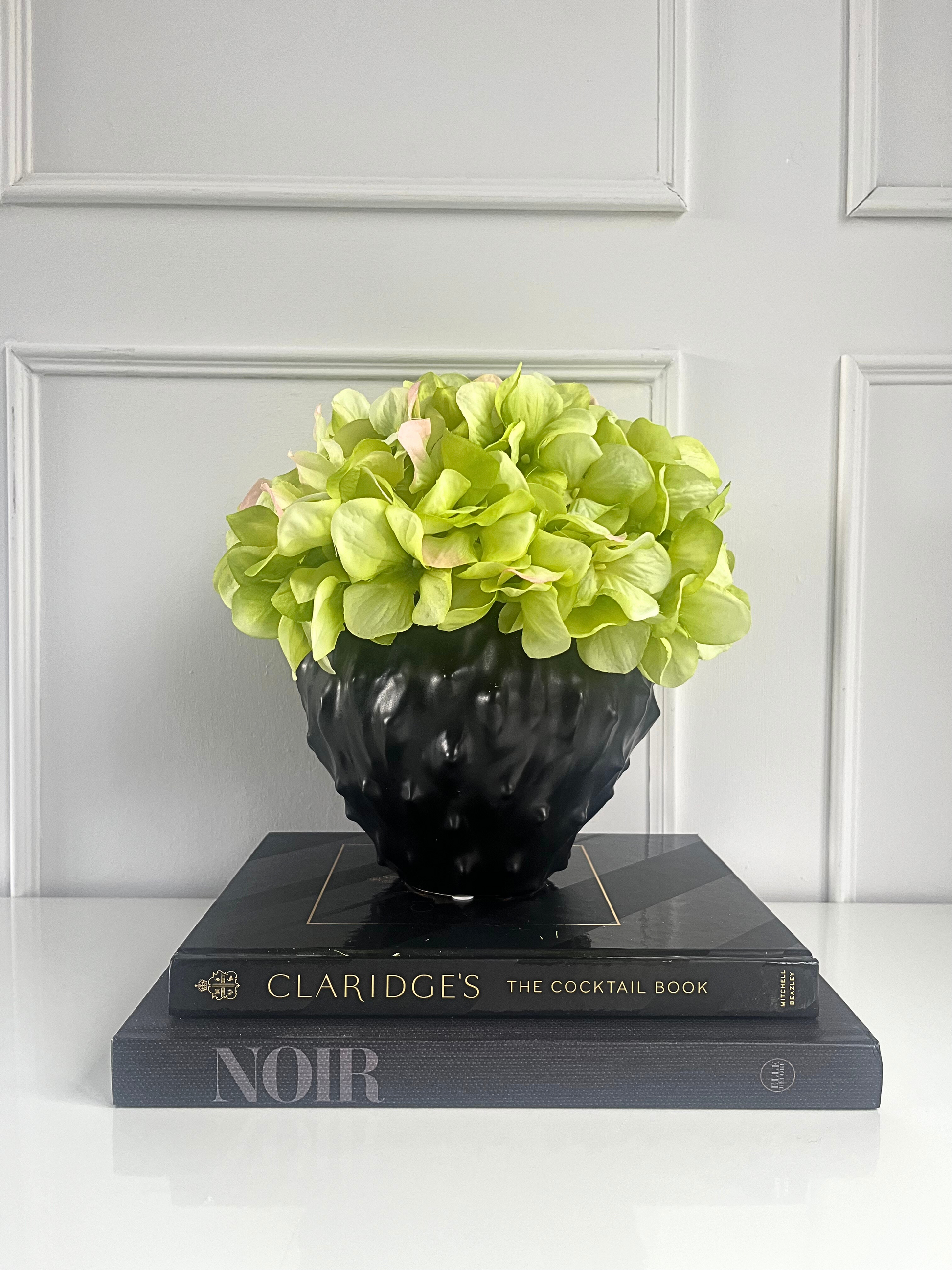 lime green artificial hydrangea set in a black spiky planter displayed on a stack of books.