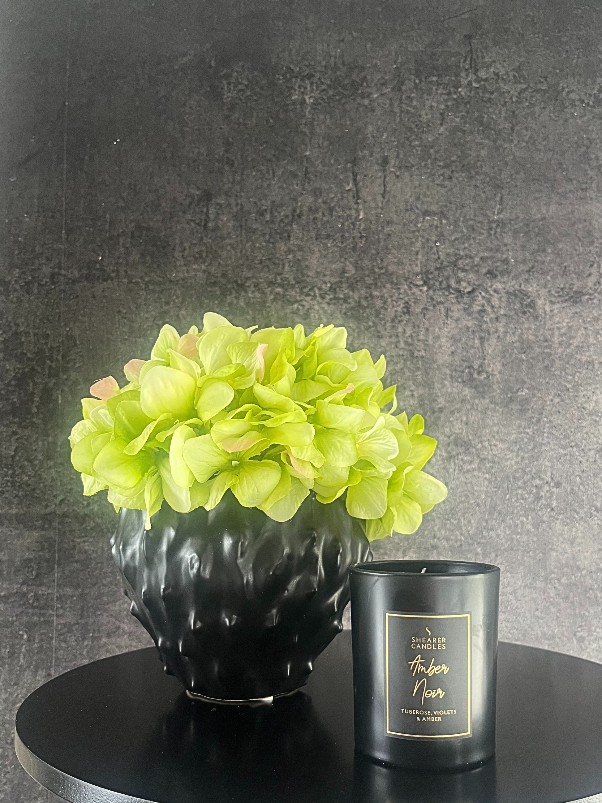 lime green artificial hydrangea set in a black spiky planter displayed on a table next to a black candle.