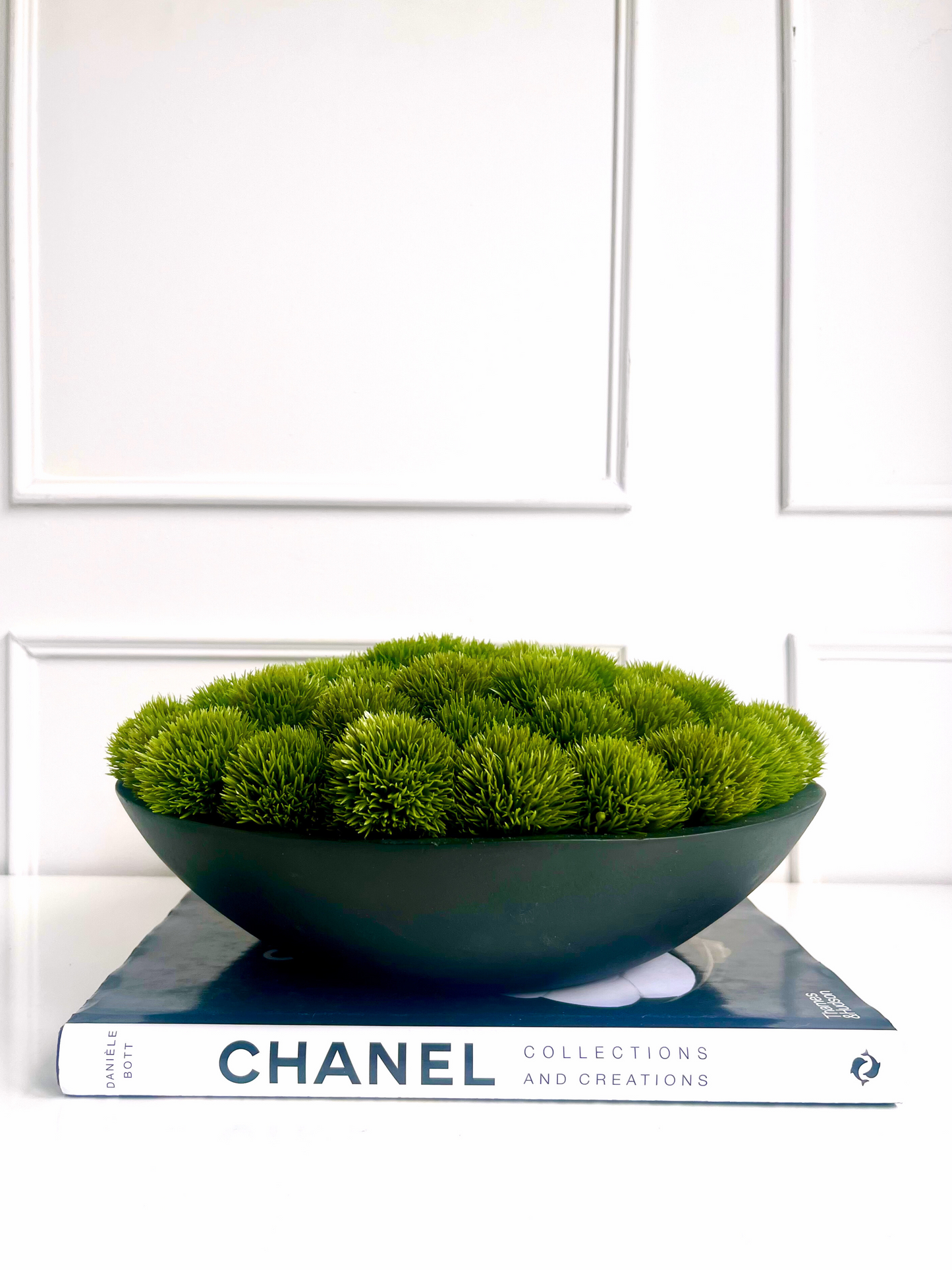 Artificial dianthus set in a black mango wood planter displayed on a book.