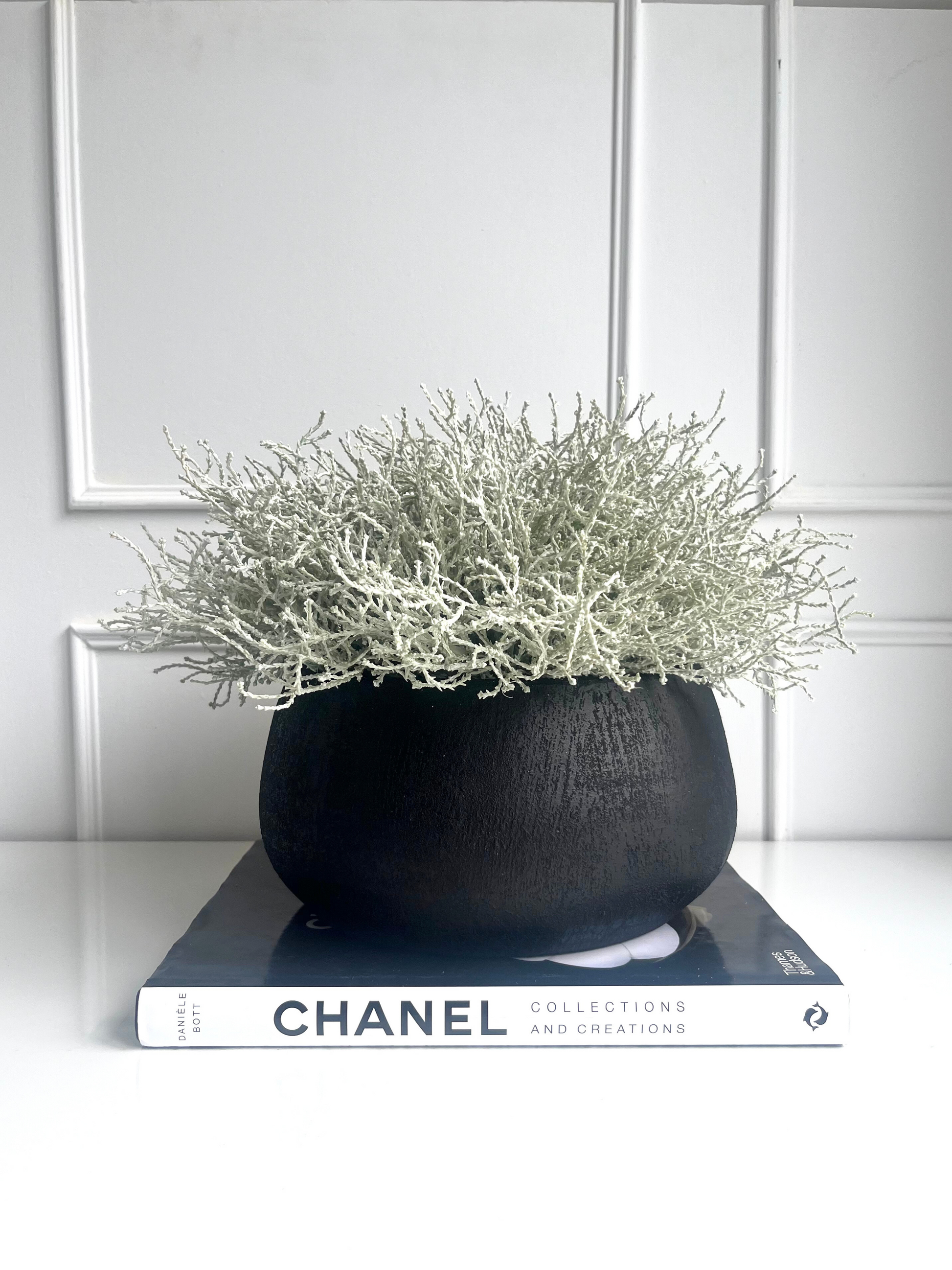 Silver grey artificial santolina set in a black melange terracotta bowl planter displayed on a book.