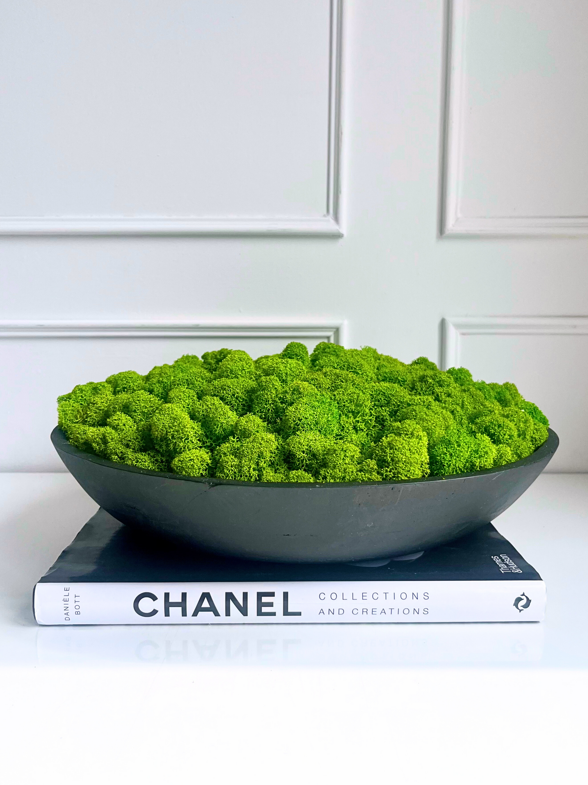 Vibrant green preserved reindeer moss set in a black mango wooden bowl displayed on a book.