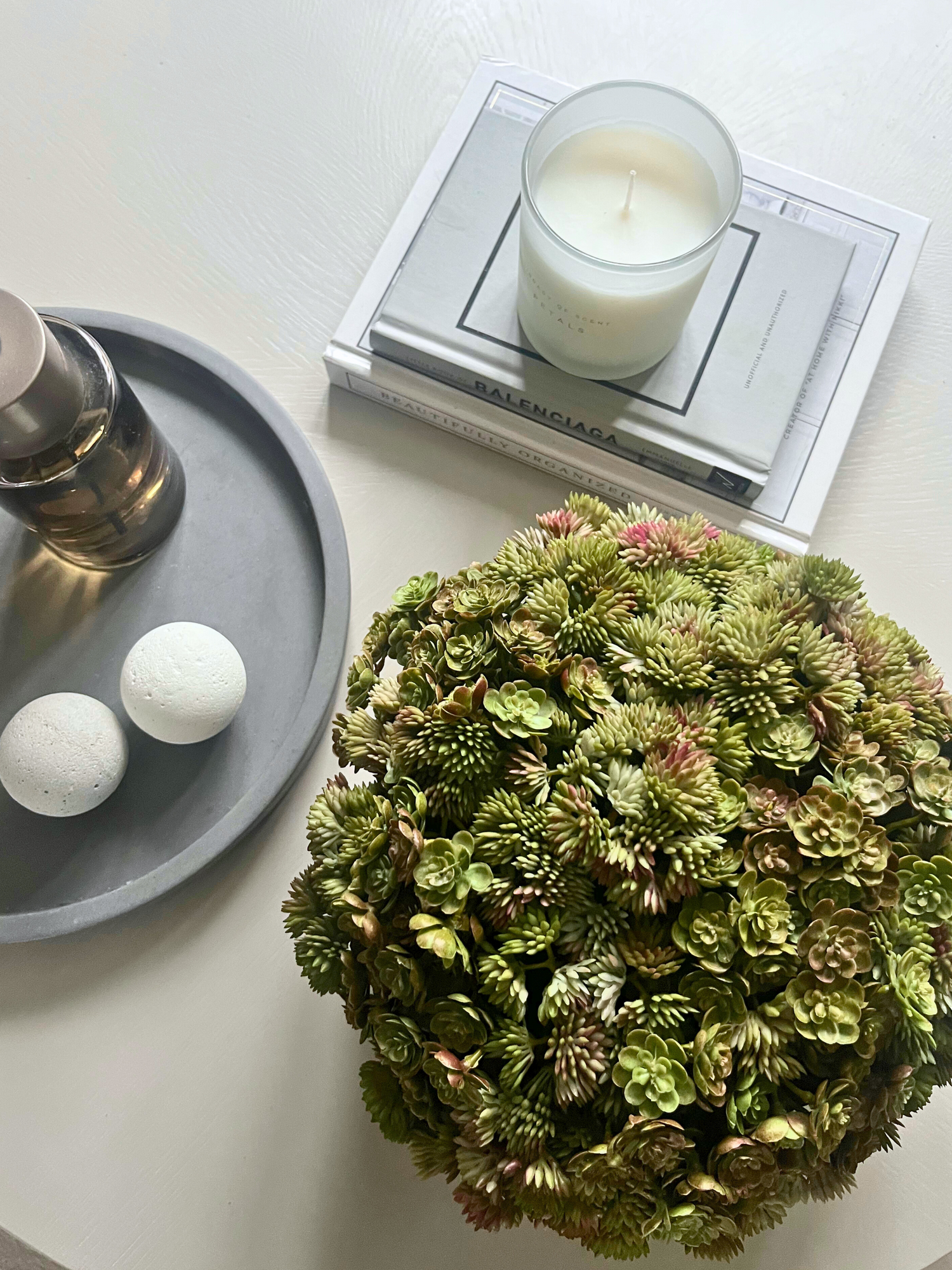 Artificial mixed succulents set in concrete bowl planter displayed on a table with a candle, books, diffuser on a tray with decorative balls.