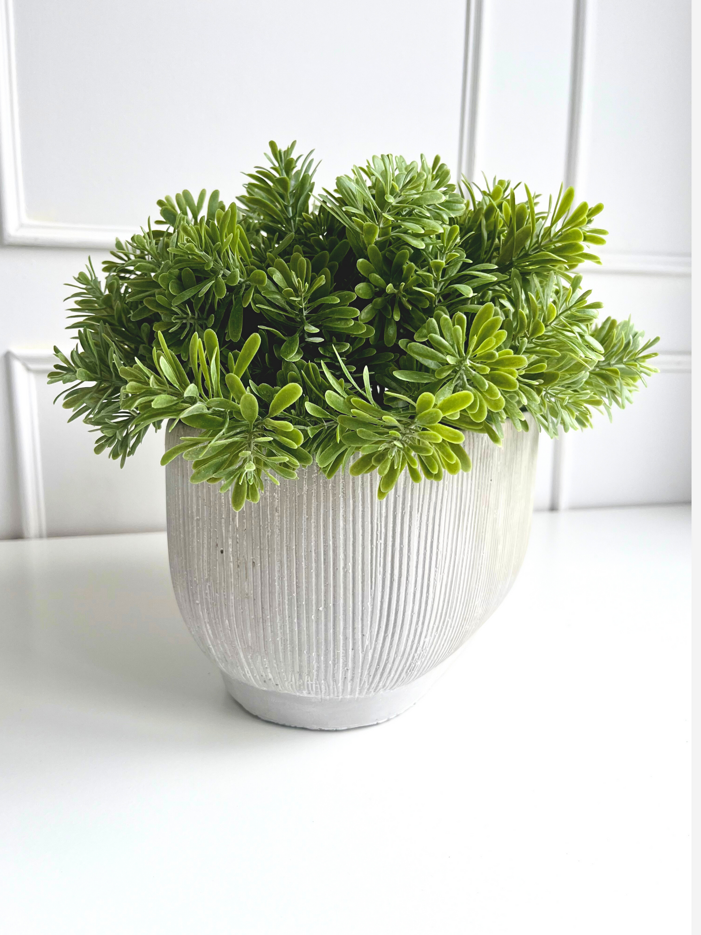 soft green artificial crossestephium succulent set in a light grey ribbed oval concrete planter.