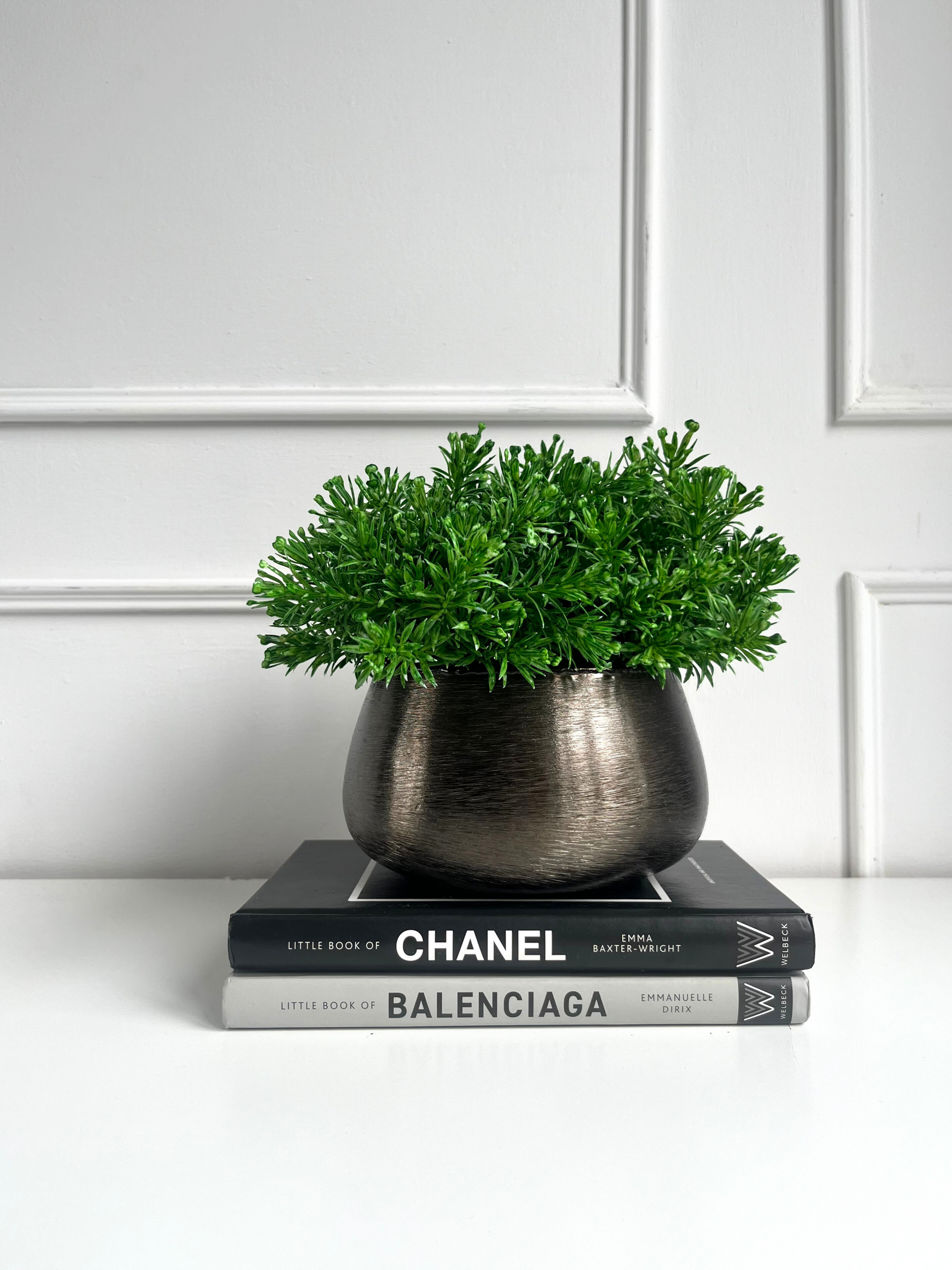 vibrant green artificial senecio set in a brushed metal bronze coloured planter displayed on a stack of books.