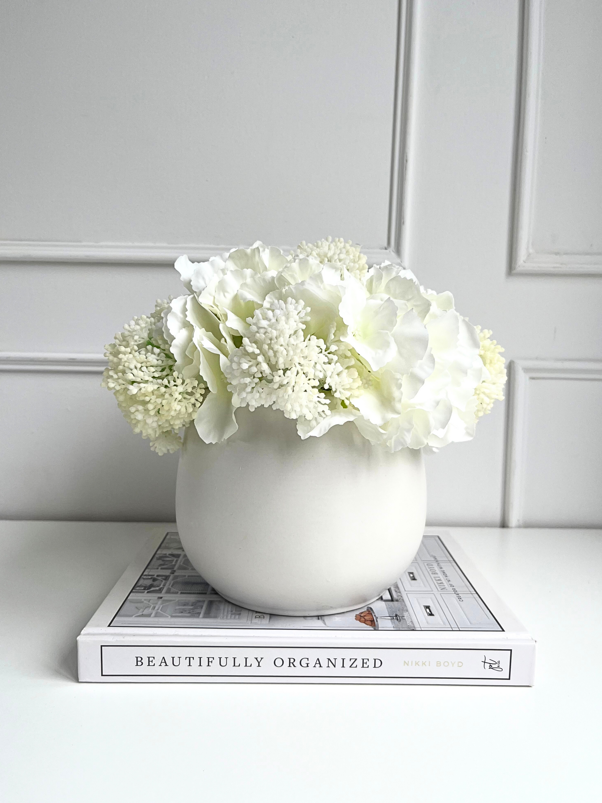 soft white artificial hydrangea and viburnum set in a matt white planter displayed on a book.