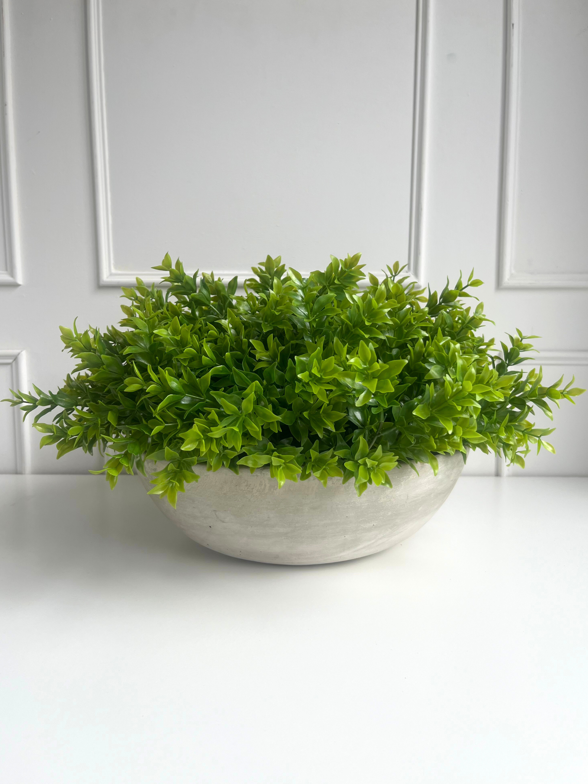 Lush green artificial tea tree plant arranged in a large light grey concrete bowl planter.