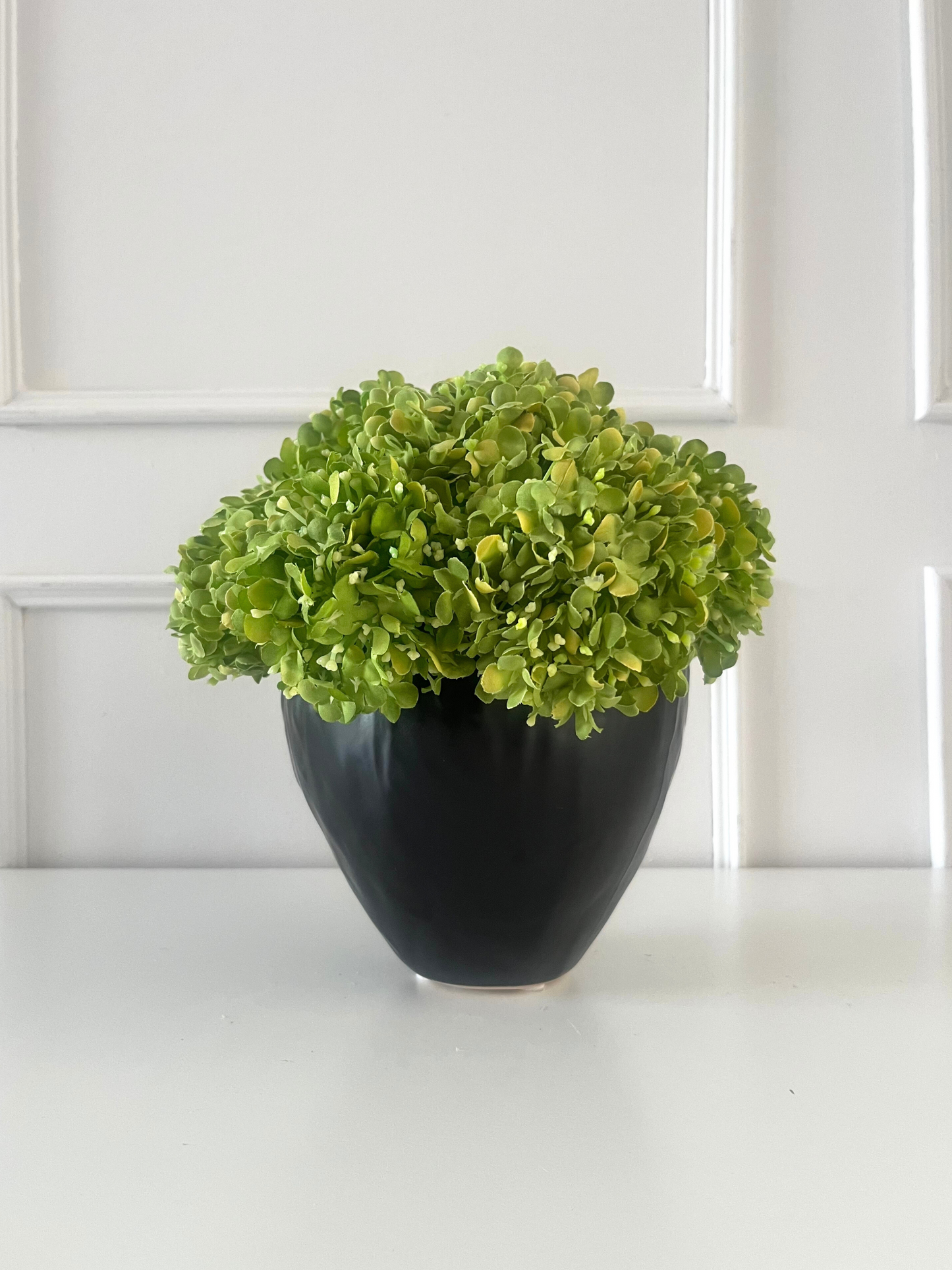 Vibrant green artificial snowball viburnum arranged in a black stoneware pot.