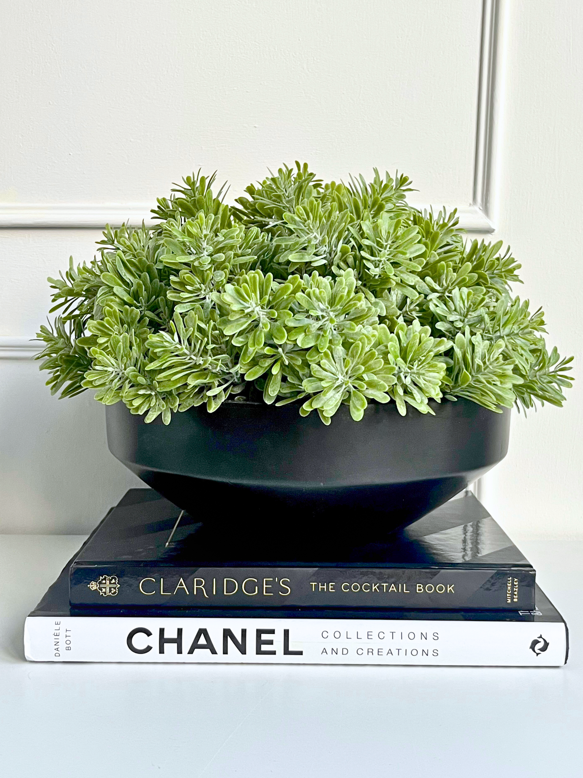 Artificial crossestephium succulent set in a black mango wood bowl planter displayed on a stack of books.