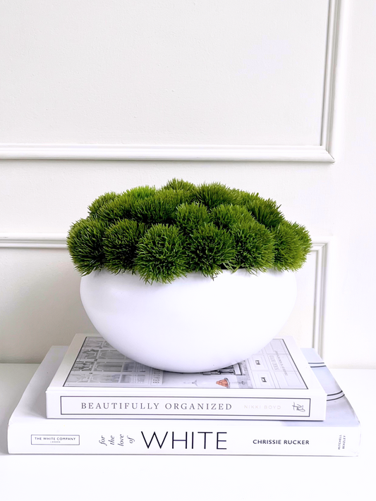 Vibrant green artificial dianthus displayed in a matt white ceramic bowl planter displayed on a stack of books