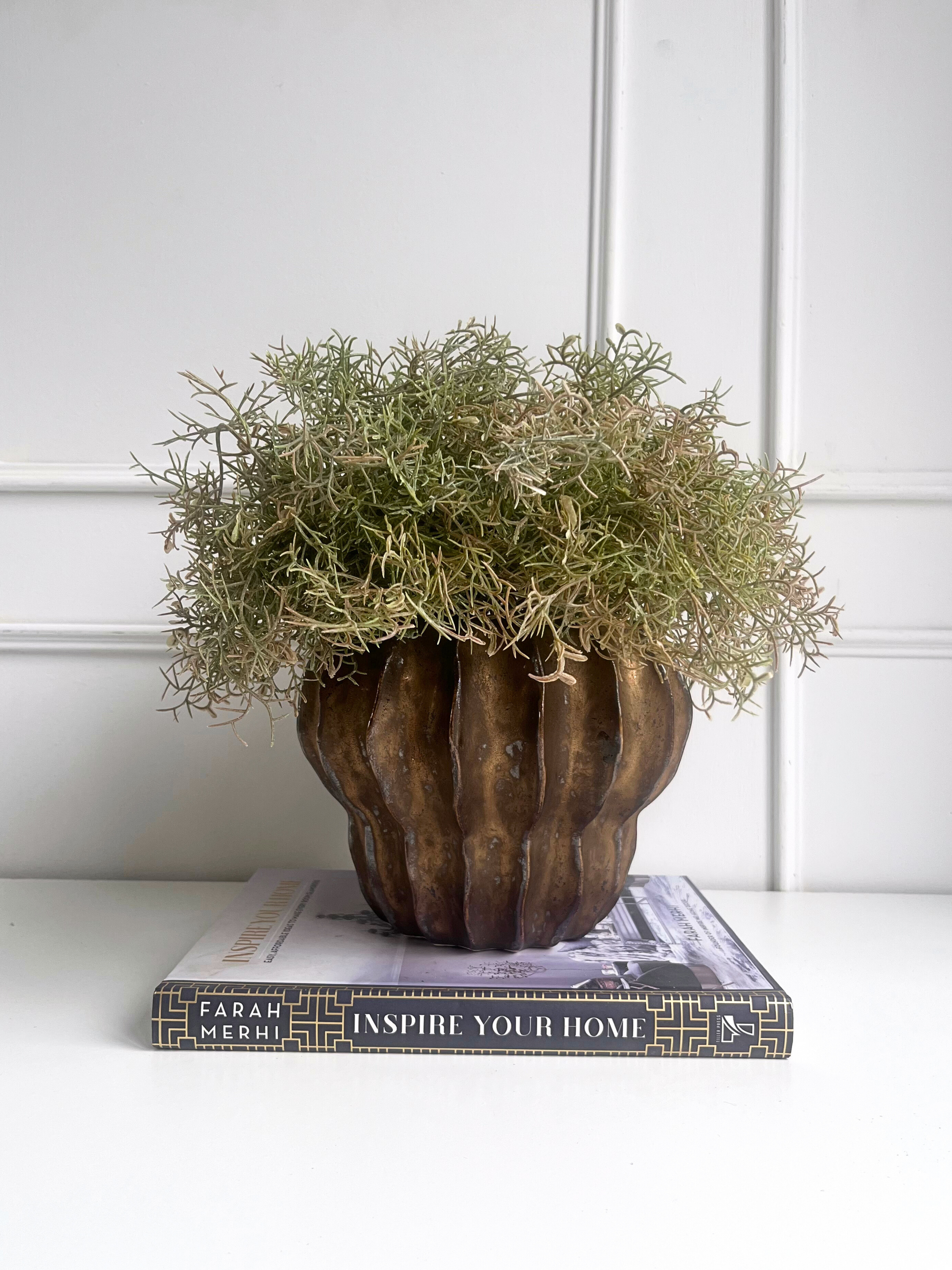 Artificial brown/green spanish moss set in a bronze coloured ridged pot displayed on a book.