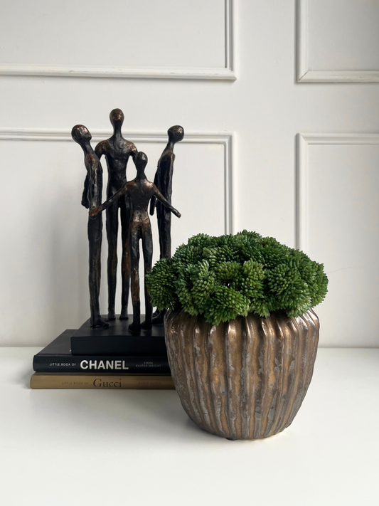 lush green artificial sedum set in a antique bronze finish ridged pot displayed next to a bronze statue on a stack of books.