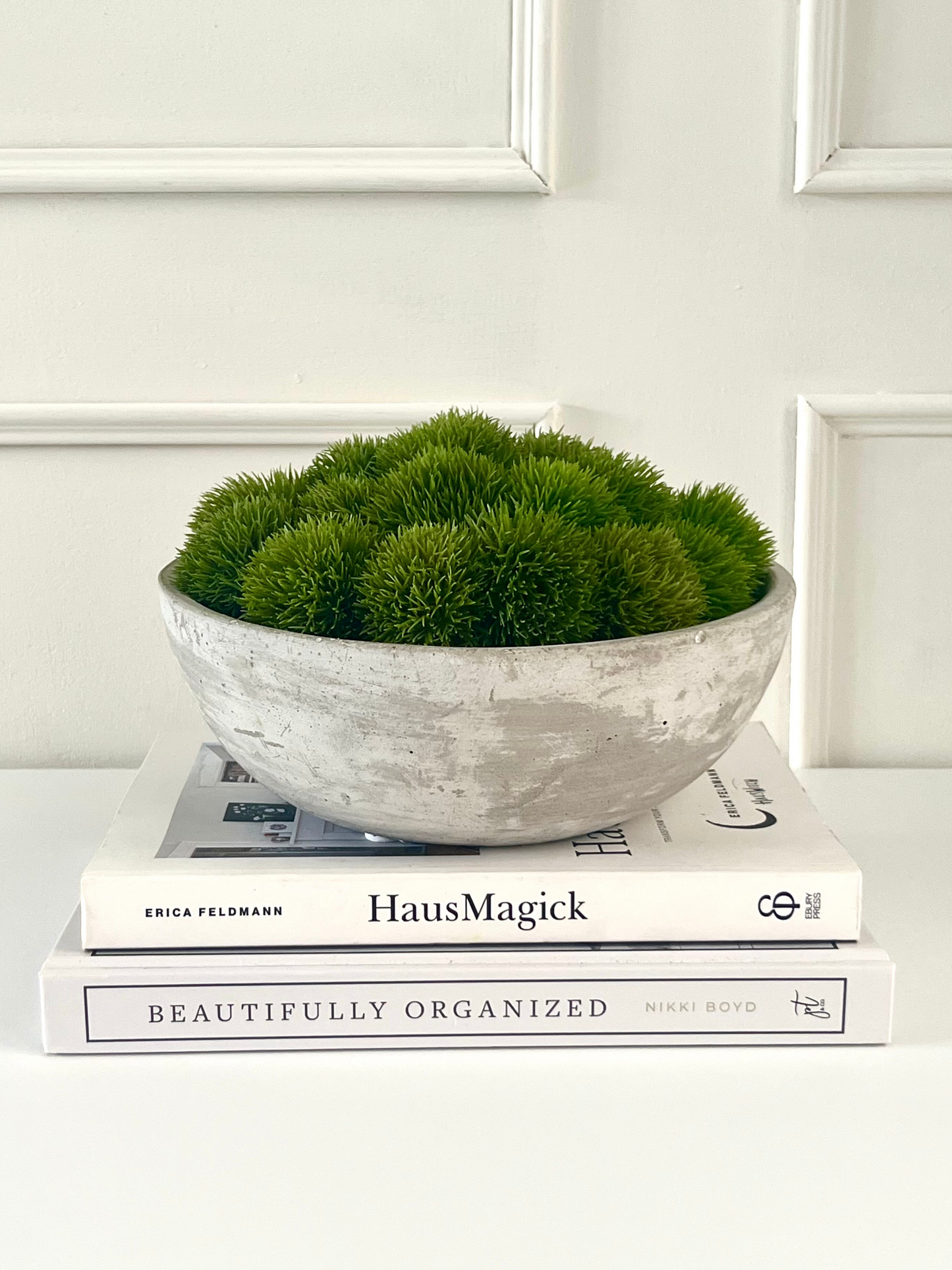 artificial dianthus arranged in a small concrete bowl planter displayed on a stack of books.