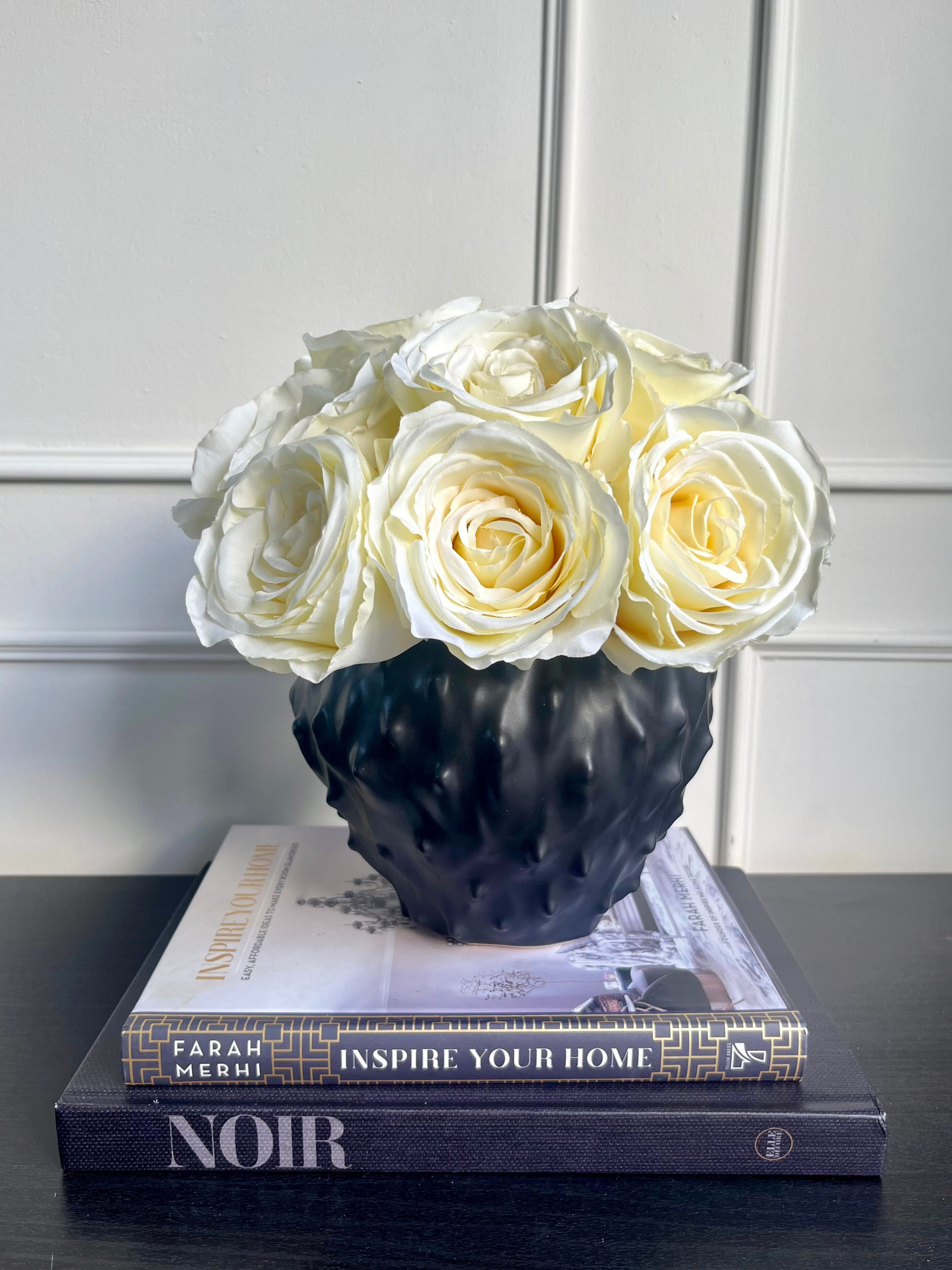 soft cream artificial roses set in a contemporary black spiky vase displayed on a stack of books.